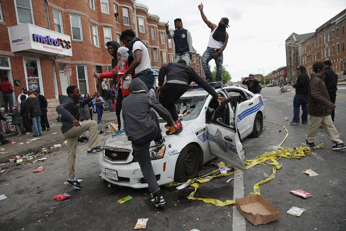During a riot, youths destroy a police car